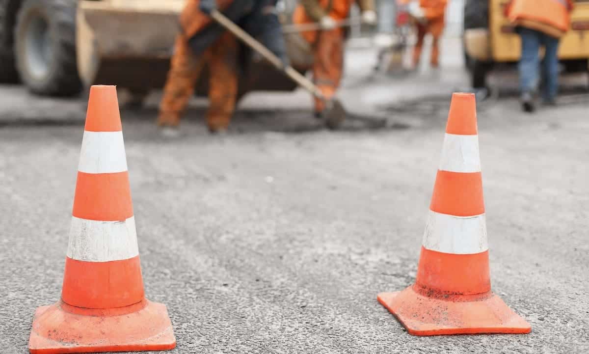 road workers repairing the road with shovels, dub asphalt with shovels at the back, the cones in the foreground