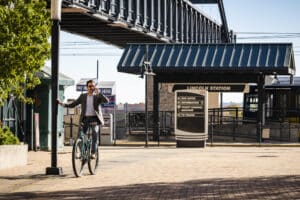 A person standing with a bicycle, talking on a phone at Lincoln Station, with signage for buses and trains visible in the background.